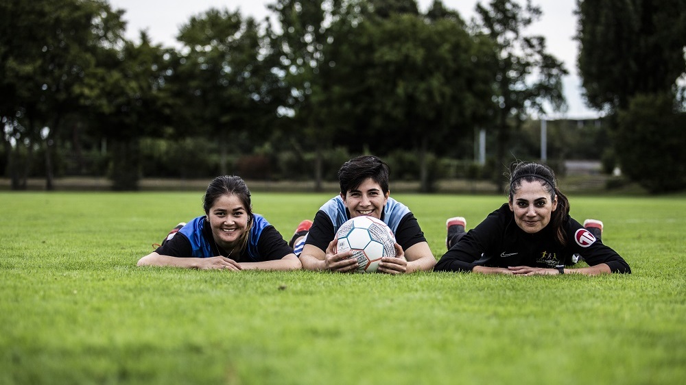 Drei Mädchen liegen auf dem Fußballfeld und lächeln