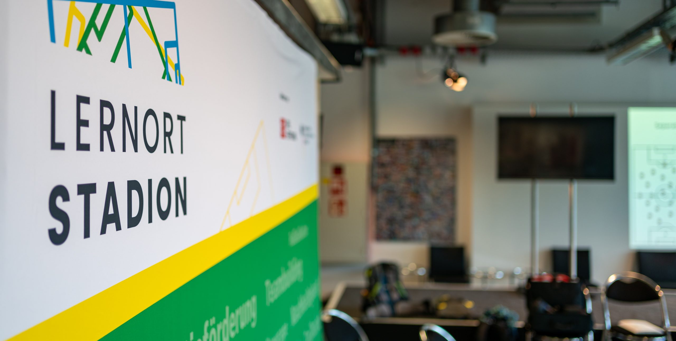 "Banner mit der Aufschrift 'Lernort Stadion' im Innenraum einer Veranstaltungshalle, die für Workshops der DFL Stiftung genutzt wird."