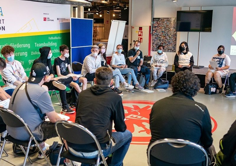 Die Teilnehmenden sitzen auf den Stühlen in einem Kreis.