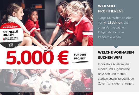 Eine Gruppe junger Menschen spielt Fußball, während im Vordergrund ein rotes Banner mit der Aufschrift 