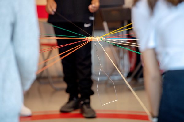 Man sieht Hände, die mit Teamwork einen Gegenstand an Fäden in der Luft halten