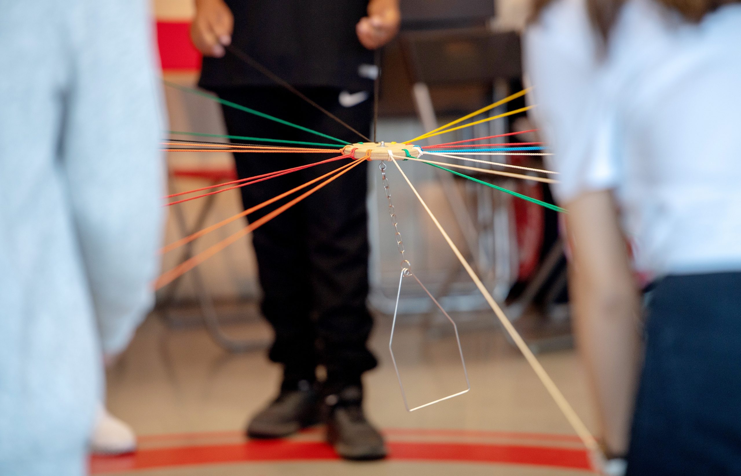 Man sieht Hände, die mit Teamwork einen Gegenstand an Fäden in der Luft halten