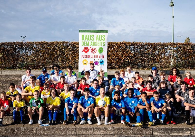 Die Teilnahmenden in Trikots verschiedener Farben sitzen auf der Tribüne.
