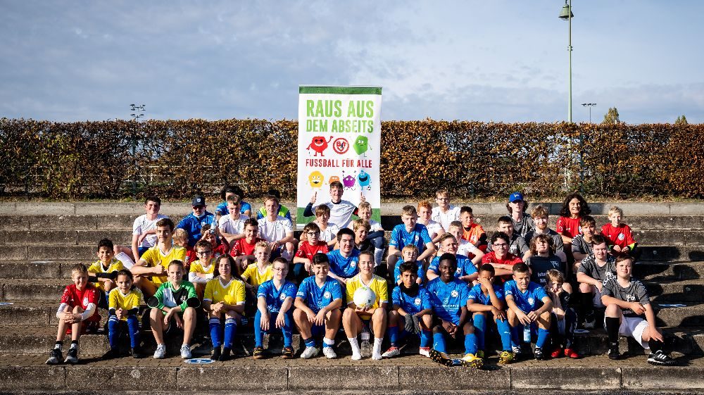 Die Teilnahmenden in Trikots verschiedener Farben sitzen auf der Tribüne.