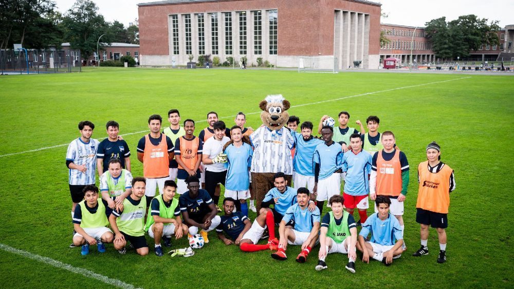 Die Teilnehmende des Abschlussturniers stehen mit der Maskotte auf dem Fußballfeld.