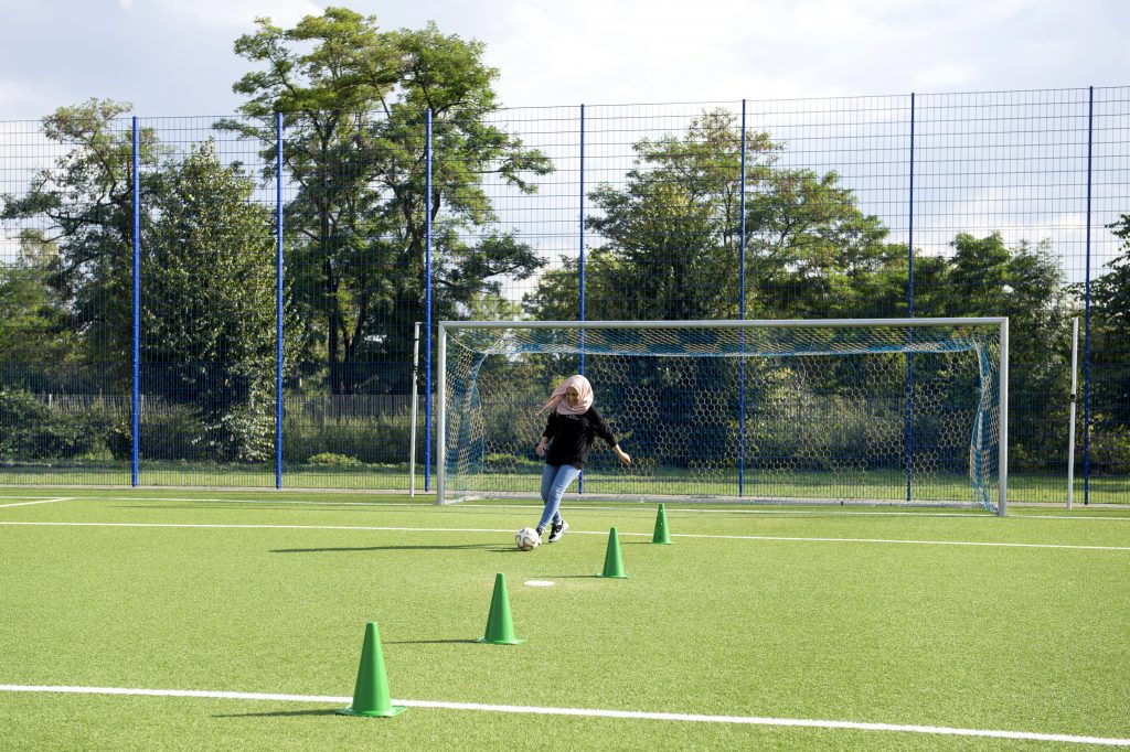 Mädchen mit rosa Kopftuch spielt Fußball auf dem Fußballfeld.