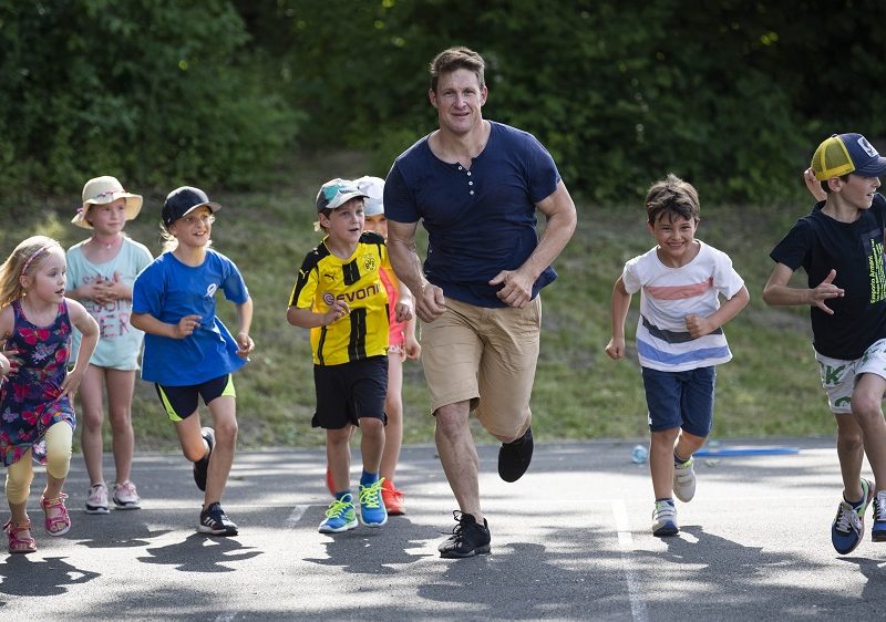 Matthias Steiner (Kurator der DFL Stiftung) und neun Kinder laufen nebeneinander auf einer Tartanbahn.