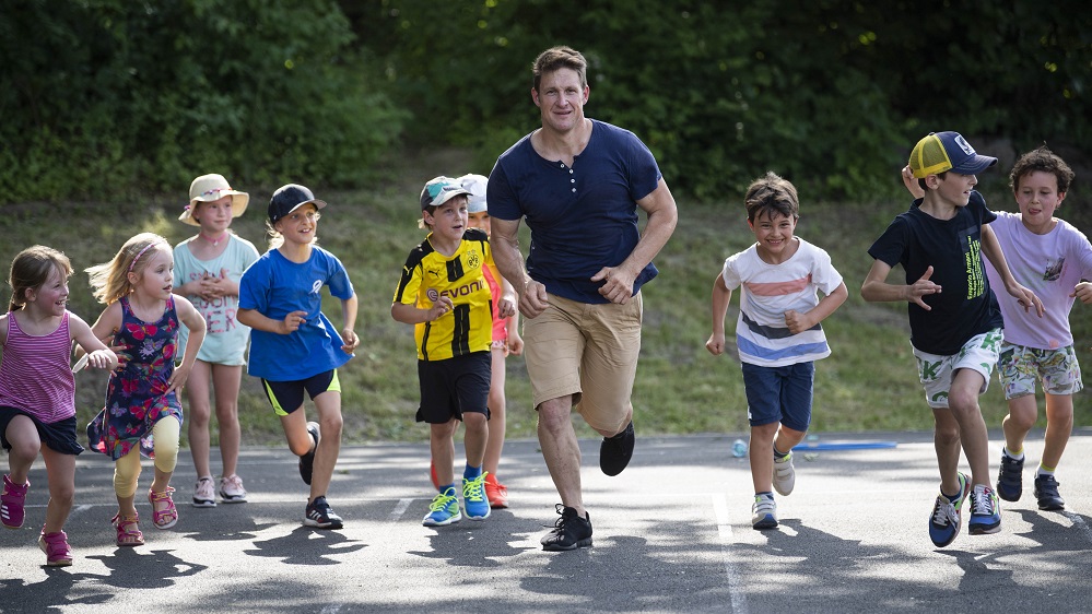 Matthias Steiner (Kurator der DFL Stiftung) und neun Kinder laufen nebeneinander auf einer Tartanbahn.
