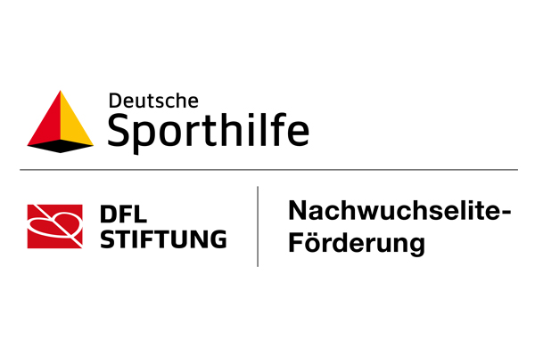 Eine Gruppe von sieben Personen steht auf einer Bühne vor einem großen Bildschirm mit der Aufschrift "Übergabe der Kapitänsbinde". Die Personen halten jeweils gerahmte Bilder oder andere Auszeichnungen in den Händen. Im Hintergrund ist ein Fußballfeld und die Aufschrift "Lerntort Stadion" zu sehen.