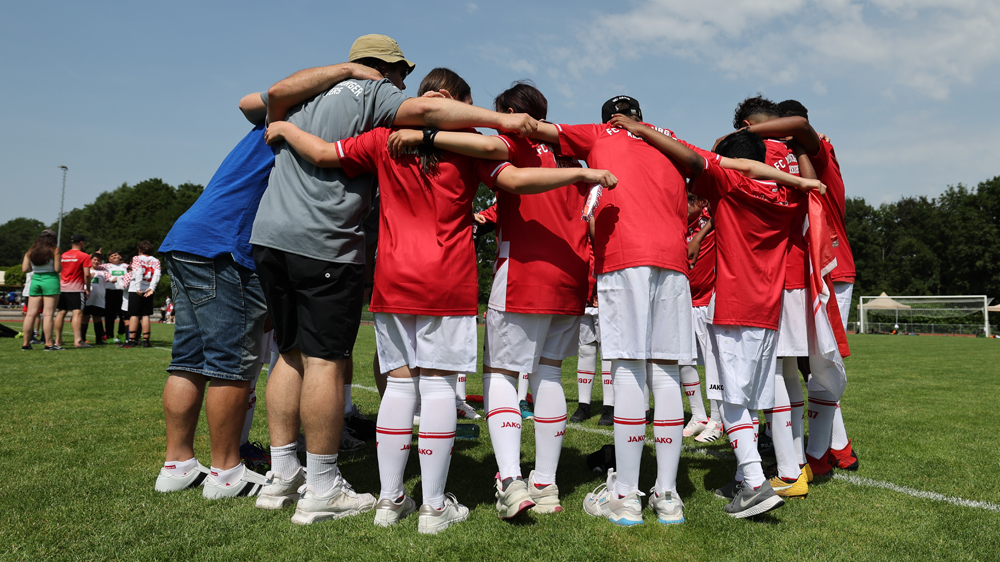 Ein Team steht im Kreis. Die Spielerinnen und Spieler haben die Arme über die Schultern gelegt.