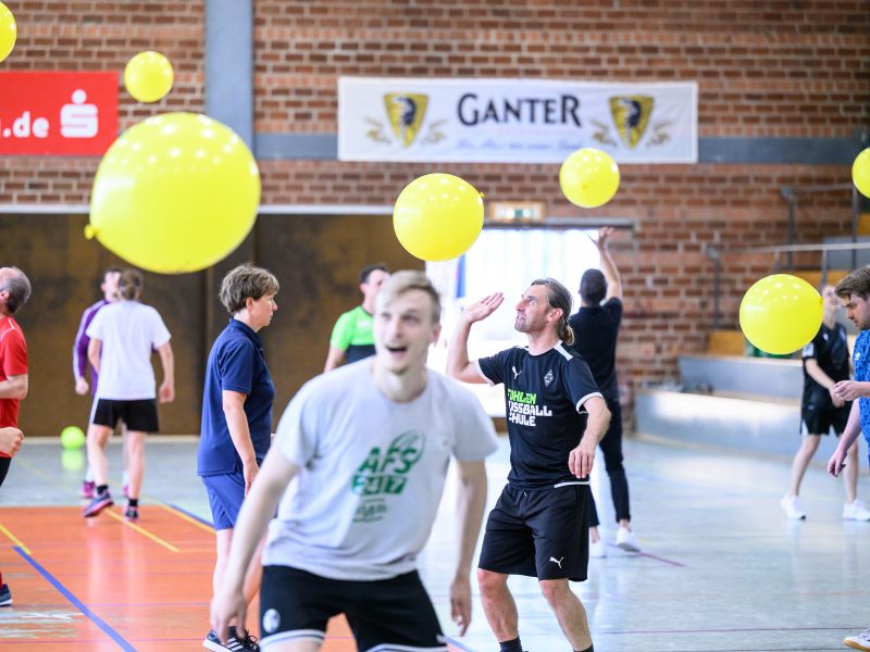 Drei begeisterte Fußballspieler im grünen Trikot stehen auf einem Podest und freuen sich, vermutlich über einen Gewinn beim FußballFreunde-Cup Nordost 2018. Im Hintergrund sind Werbebanner und das Spielfeld zu sehen.