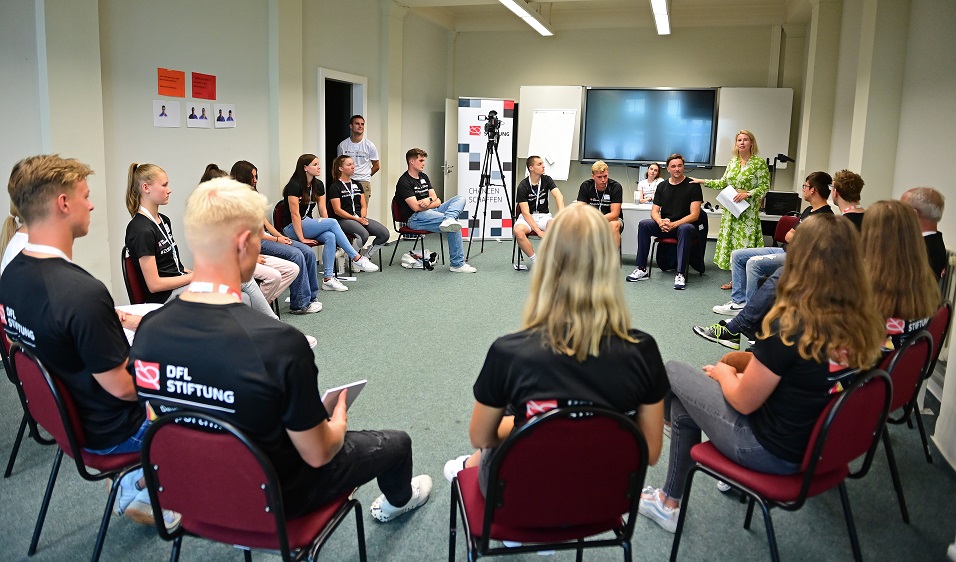 Die Athlet:innen sitzen im Stuhlkreis und hören der Referierenden zu.