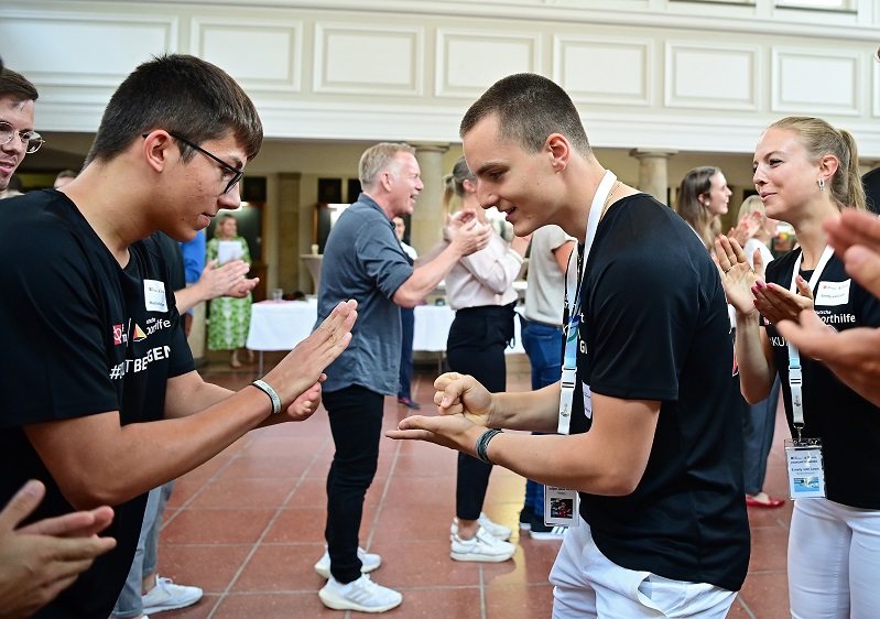 Mehrere Personen sind zu sehen, die Schnick-Schnack-Schnuck spielen und dabei angefeuert werden.
