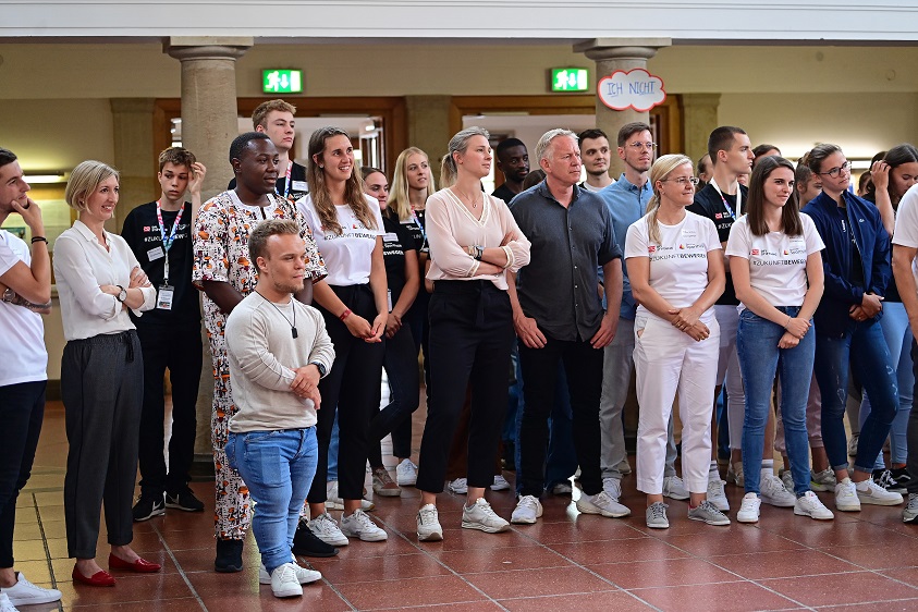 Mehrere Personen stehen auf einer Seite und blicken nach vorne.