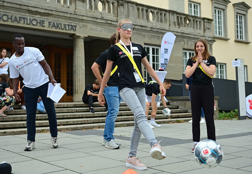 Eine Person schießt mit verbundenen Augen einen Fußball.