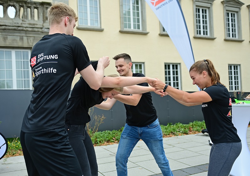 Zwei Menschen halten sich an den Händen, während zwei andere versuchen, ein T-Shirt von der einen Person auf die andere zu ziehen.