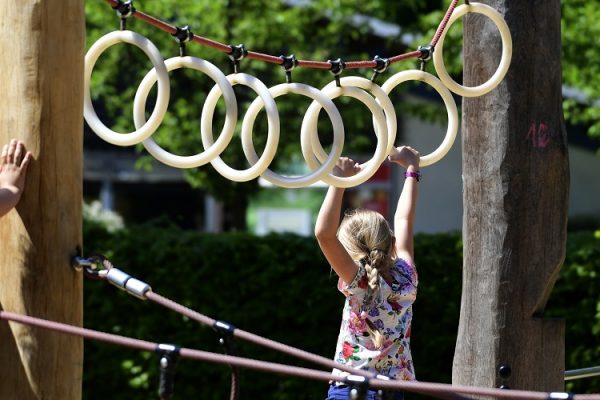 A girl shimmies along rings on a playground.