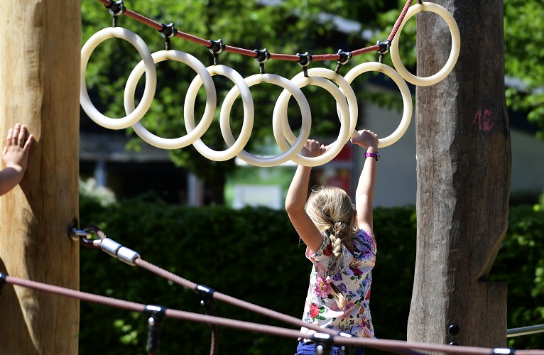 A girl shimmies along rings on a playground.