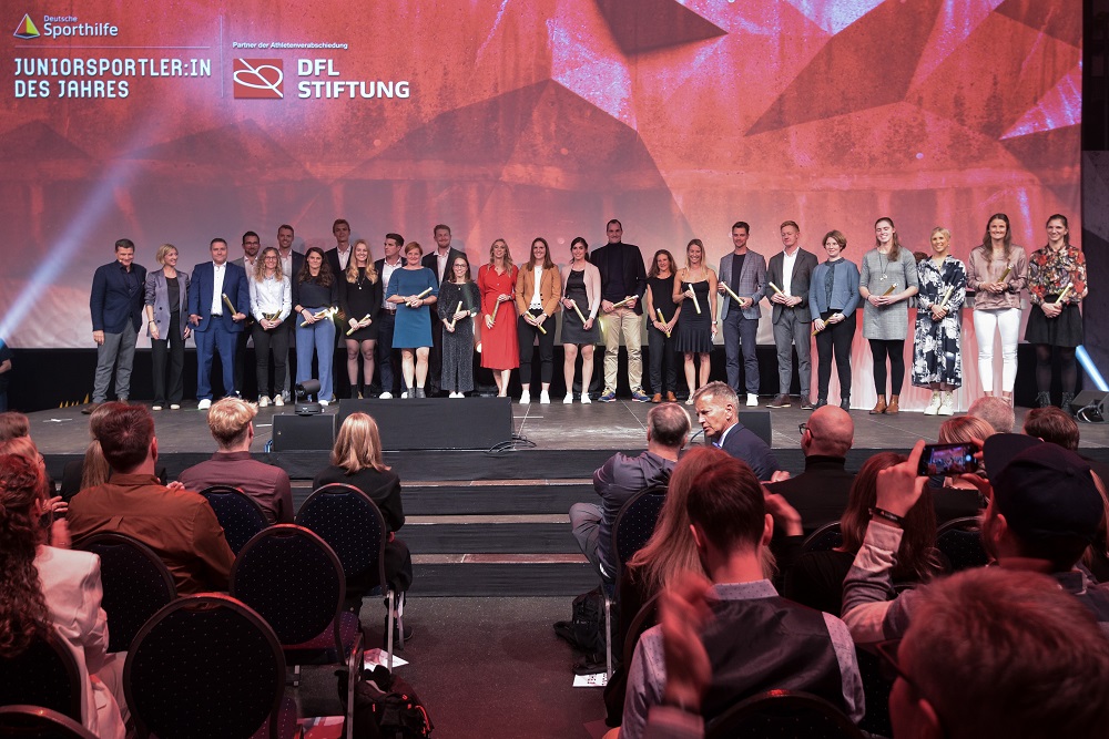 Die verabschiedeten Athlet*innen stehen nebeneinander auf einer Bühne, vor ihnen ist das Publikum.