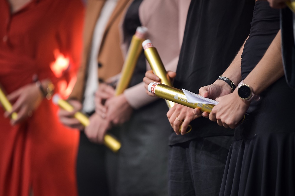 Eine Nahaufnahme von goldenen Staffelstäben, die sich in den Händen verschiedener Personen befinden.