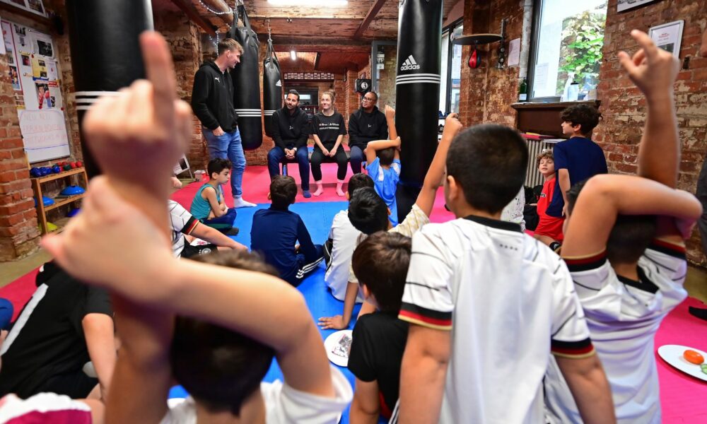 Lena Büchner, Claudio Pizarro und Paulo Sérgio sitzen zusammen auf einer Bank und bekommen viele Fragen von den Kindern gestellt.