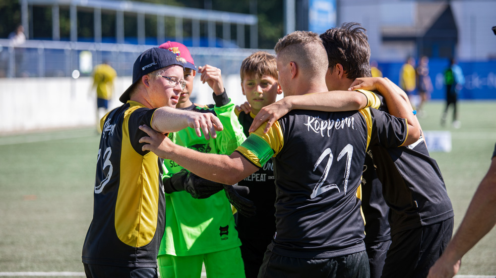 Fünf junge Fußballspieler stehen auf dem Fußballplatz im Kreis und haben die Arme über die Schultern gelegt.