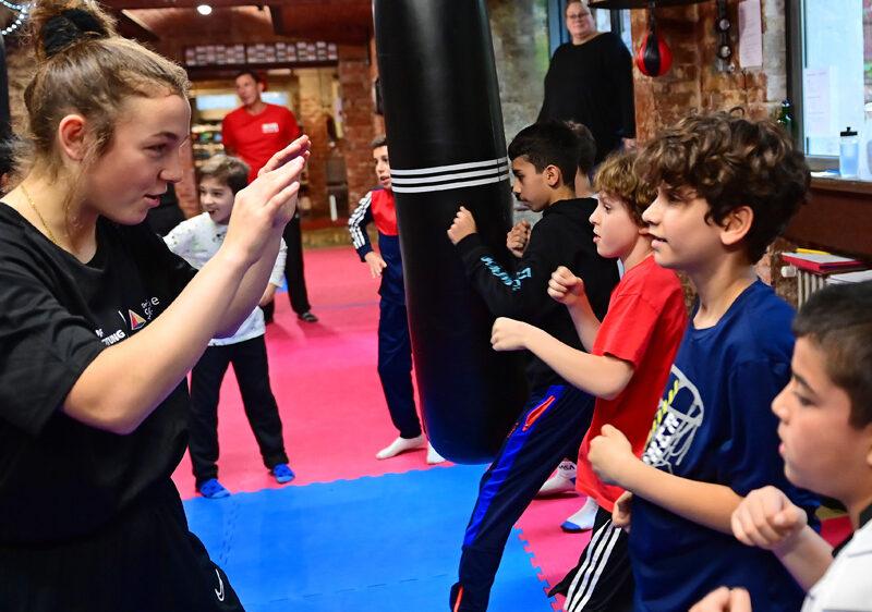 Lena Büchner (links) steht vier Jungs (rechts) in einer Boxhalle gegenüber und wehrt deren Schläge ab.