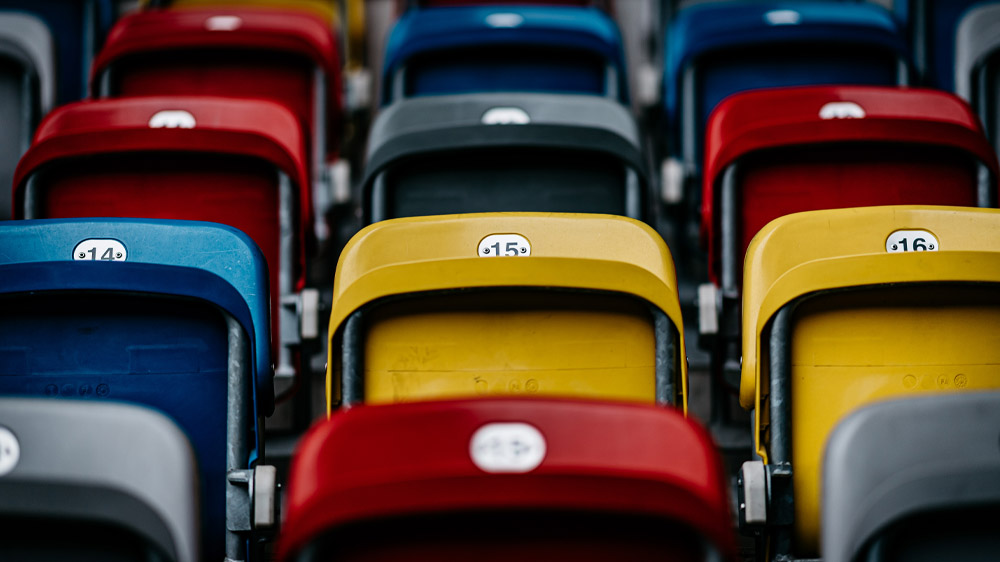 Leere Stadiontribünen in verschiedenen Farben, symbolisch für das Thema Hassrede und Diskriminierung im Fußball.