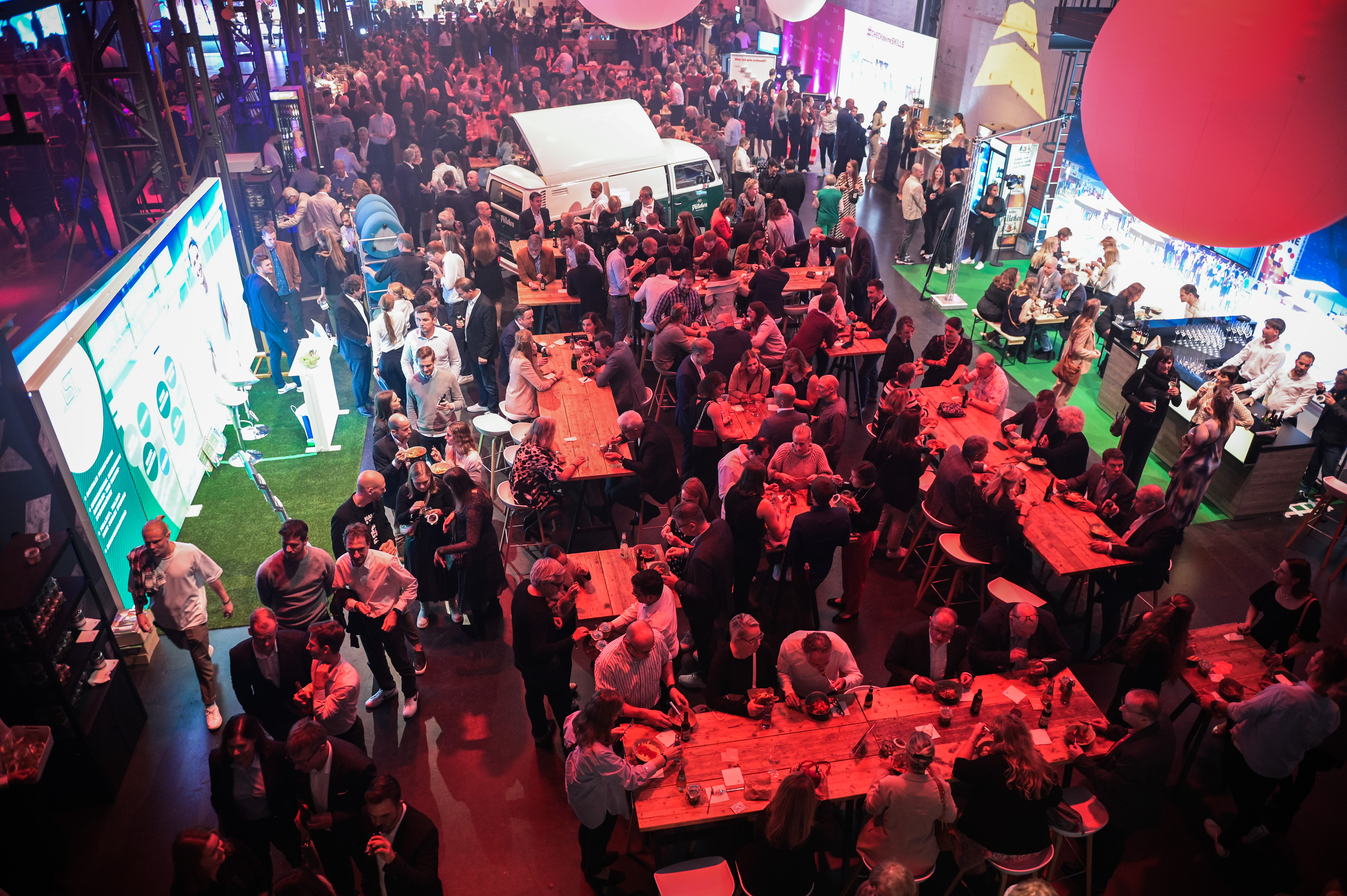 Überblick über eine festliche Veranstaltung mit zahlreichen Gästen, die sich um Tische und Stände gruppieren. Im Hintergrund eine große Bühne und Werbeflächen, die die Veranstaltung "Juniorsportler*in des Jahres 2023" bewerben.