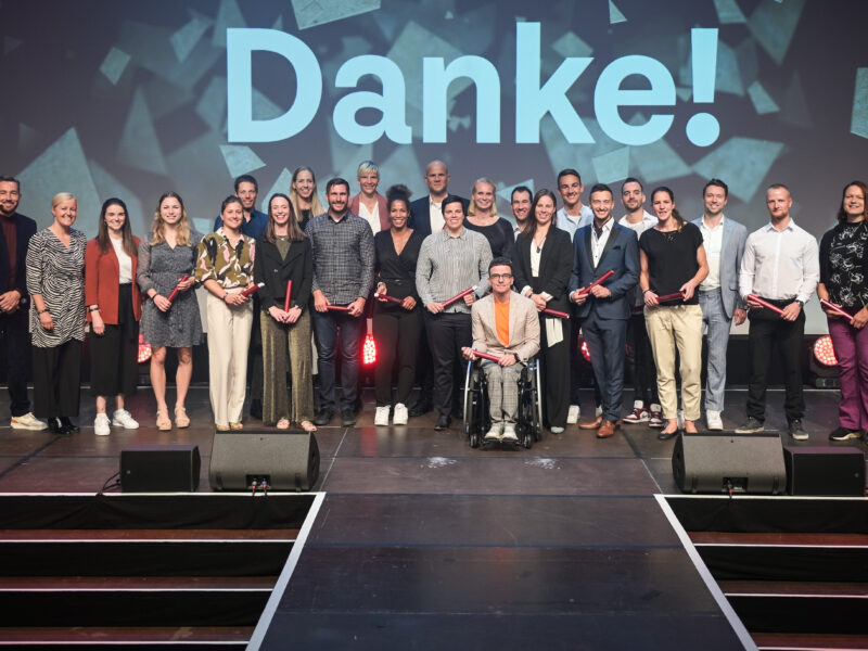 Gruppe von jungen Sportler:innen und Betreuer:innen auf der Bühne bei der Ehrung der "Sporthilfe Juniorsportler:in 2023" in Düsseldorf. Im Hintergrund steht groß "Danke!".