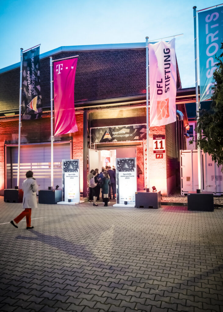 Eingangsbereich der Preisverleihung "Junior Sportler*in des Jahres 2023" in Düsseldorf, mit Personen im Hintergrund und Bannern der Deutschen Sporthilfe und der DFL Stiftung.