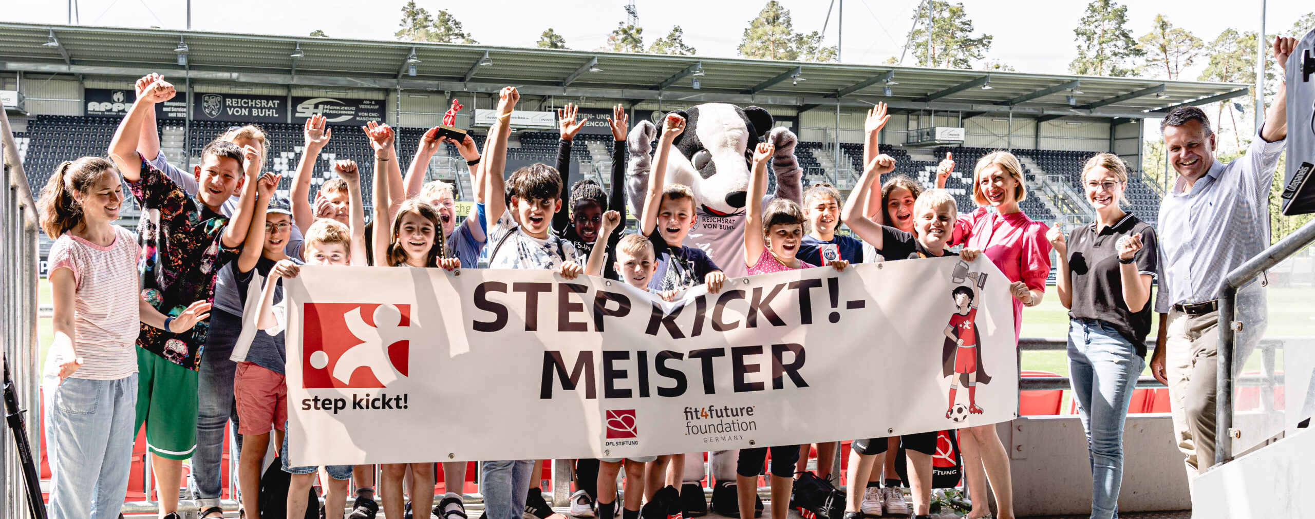 Junge Fußballspieler feiern mit erhobenen Armen und strahlenden Gesichtern den Gewinn des Turniers "step kickt!". Im Hintergrund ein großes Banner mit der Aufschrift "step kickt! - MEISTER" und dem Logo der fit4future foundation.