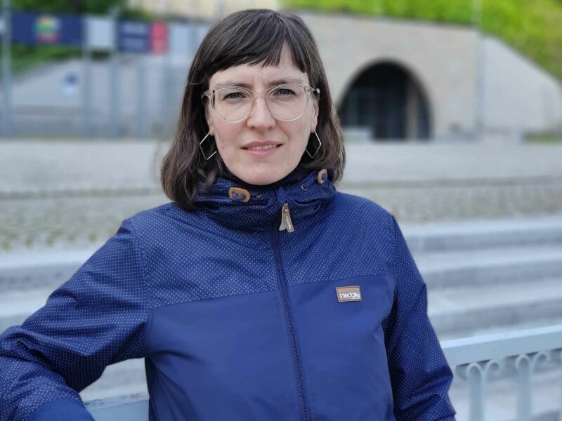 Antje Kettner, eine Frau mit Brille und dunklen Haaren, trägt eine blaue Jacke und lächelt in die Kamera.