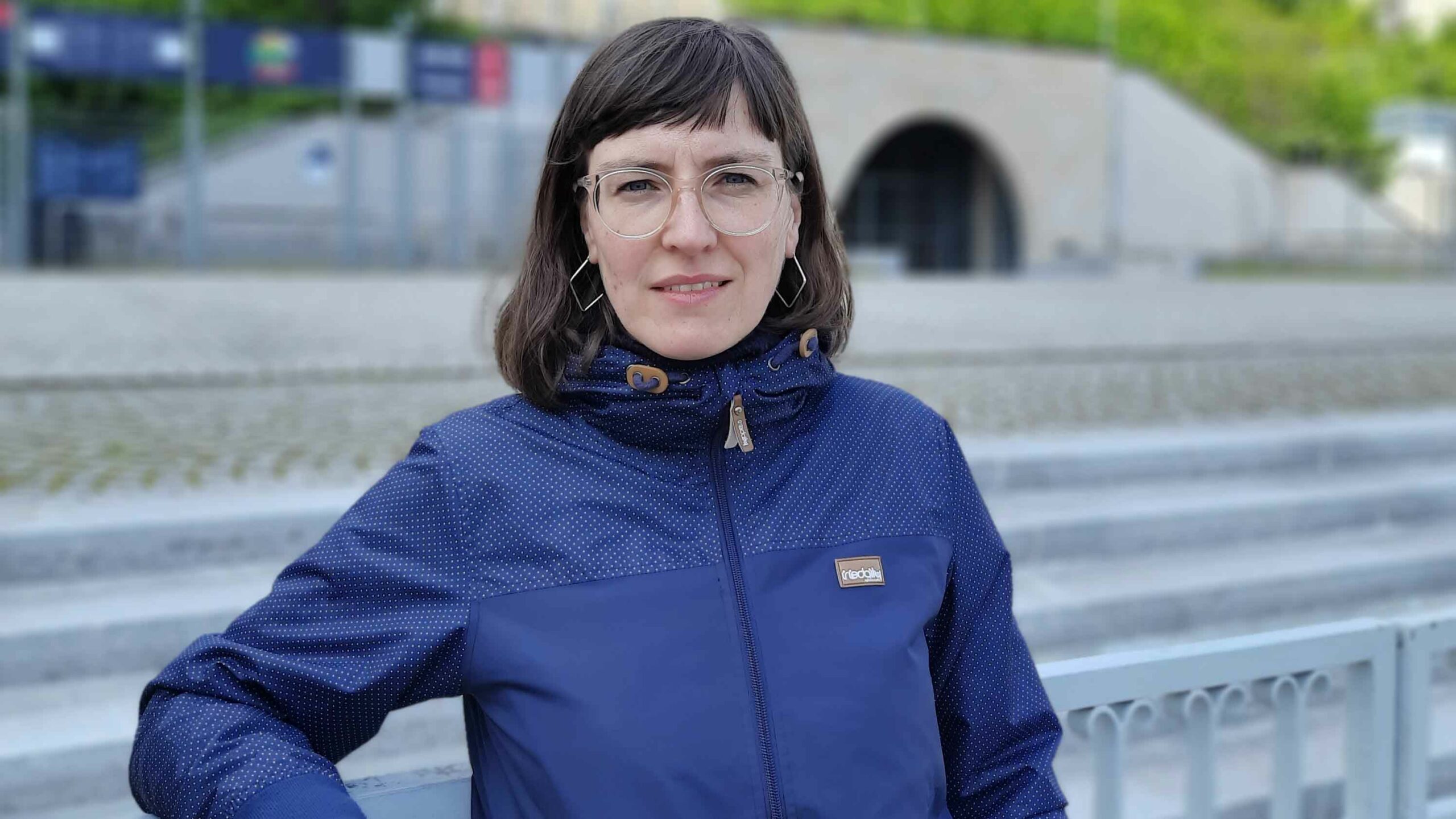 Antje Kettner, eine Frau mit Brille und dunklen Haaren, trägt eine blaue Jacke und lächelt in die Kamera.