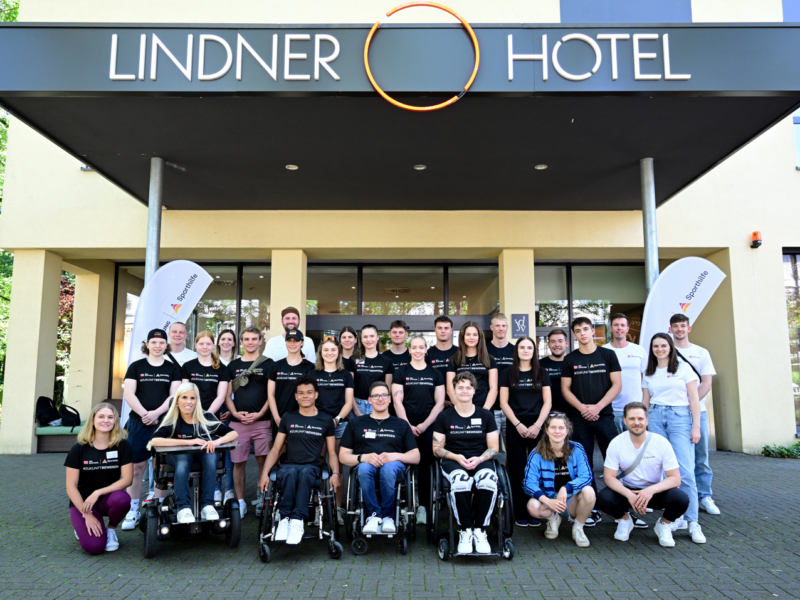 Gruppe von Menschen vor dem Hotel Lindner in Frankfurt. Einige Teilnehmer sitzen im Rollstuhl. Im Hintergrund ist die Hotelfassade mit dem Schriftzug "Lindner" zu sehen.