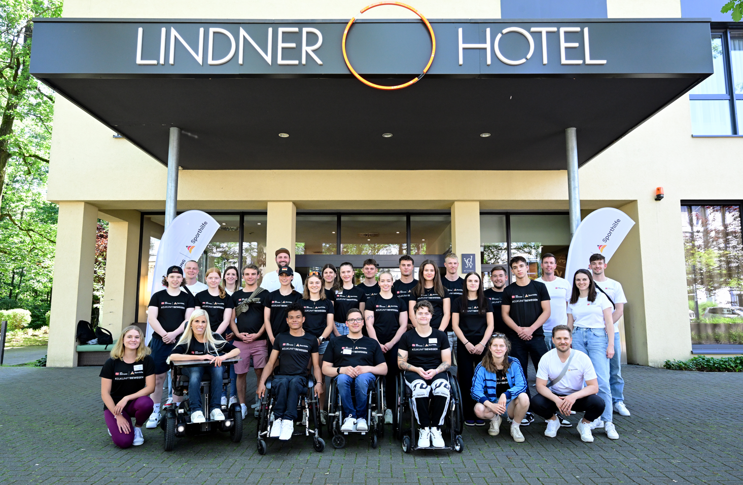 Gruppe von Menschen vor dem Hotel Lindner in Frankfurt. Einige Teilnehmer sitzen im Rollstuhl. Im Hintergrund ist die Hotelfassade mit dem Schriftzug "Lindner" zu sehen.