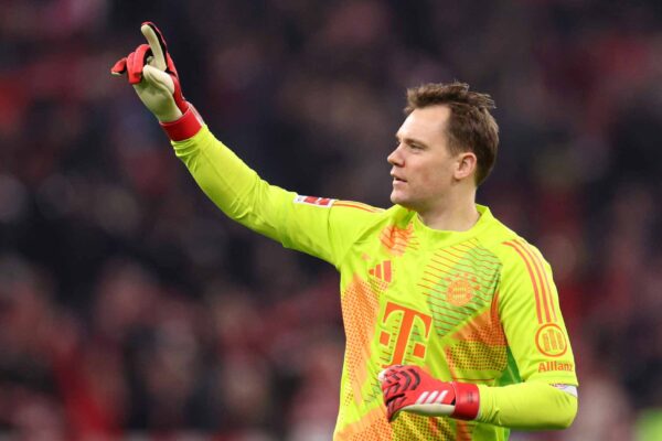Manuel Neuer, Torwart des FC Bayern München, in Aktion während eines Fußballspiels. Er trägt einen leuchtend grünen Trikot und konzentriert den Blick nach oben, die Hand zum Weisen erhoben.