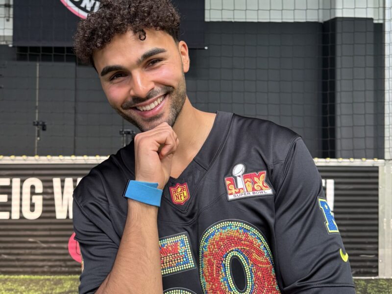 Younes Zarou, lächelnd porträtiert, trägt ein dunkelblaues Trikot mit bunten Applikationen und NFL-Logos.