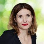 Friederike Behrends, Portraitaufnahme mit rotem Lippenstift und großen Ohrringen.